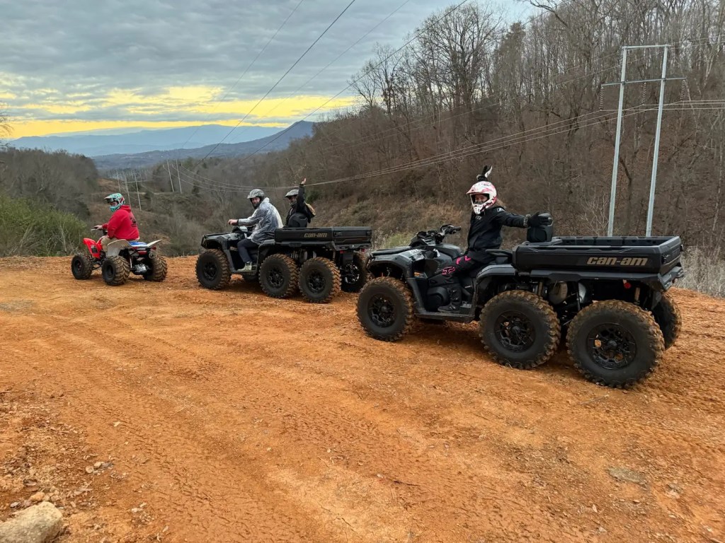 Happy family posing on Can-Am ATVs at scenic mountain overlook during guided off-road tour